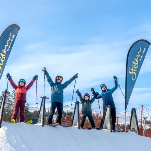 Fire børn på ski fejrer afslutningen på Stöten i Sälen med armene i vejret.