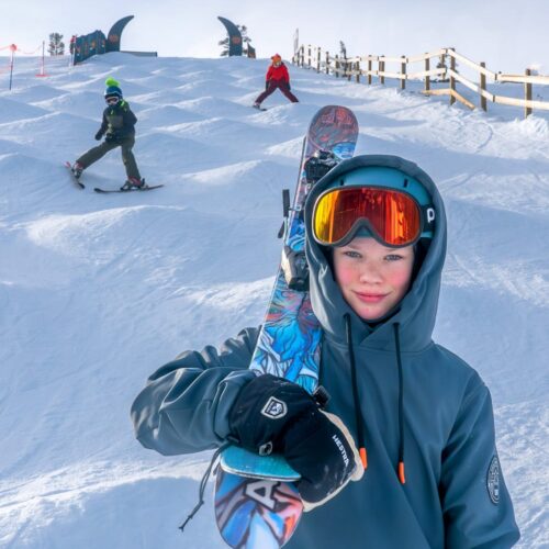 Person holding colourful skis over his shoulder in puckelpist with two skiers in the background