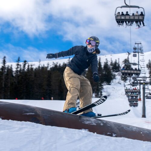 Person på ski på skinne i Stöten Snowpark med snedækkede pister og lifte i baggrunden