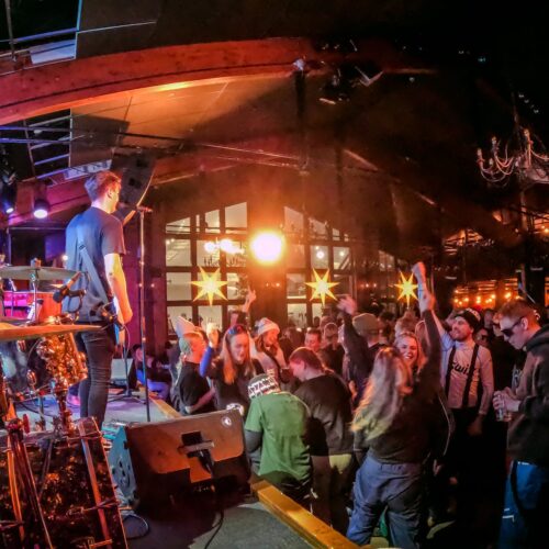 Live indoor concert with band on stage and dancing audience under colourful lights