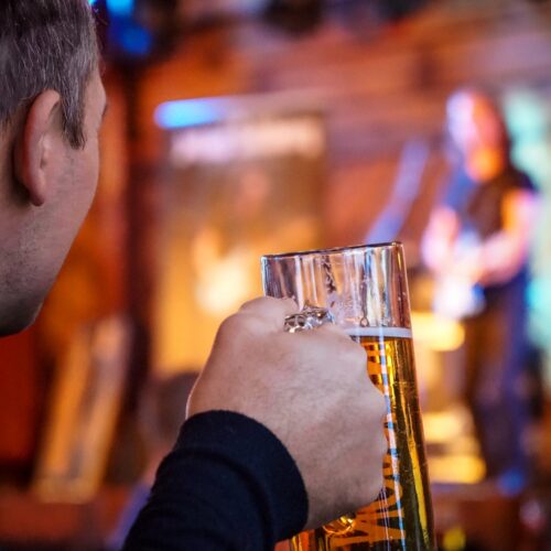Person holder ølglas og ser liveband på oplyst scene indendørs