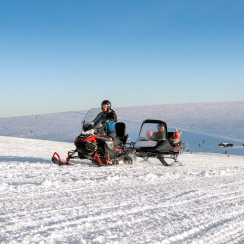Snöskoter med pulka transporterar barn över vidsträckt fjäll, klar vinterdag