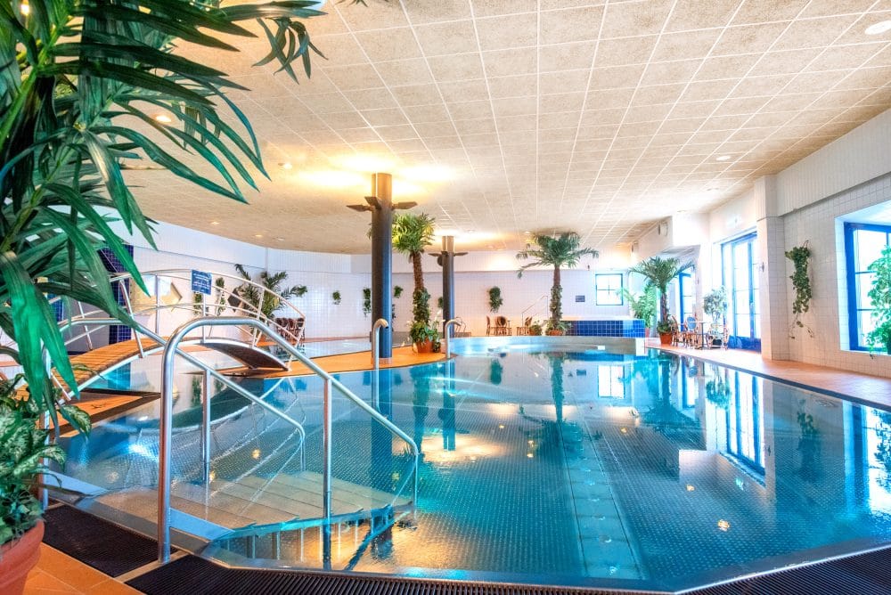 Inomhuspool med bro, palmer och ljus belysning i spa-miljö