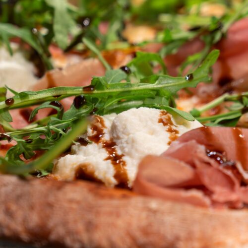 Close-up of pizza with air-dried ham, rocket, mozzarella and balsamic vinegar on a crispy base.