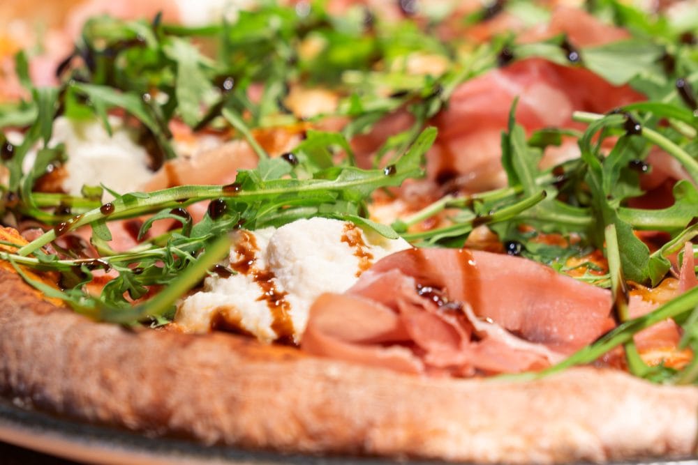 Close-up of pizza topped with air-dried ham, rocket, mozzarella and balsamic vinegar.