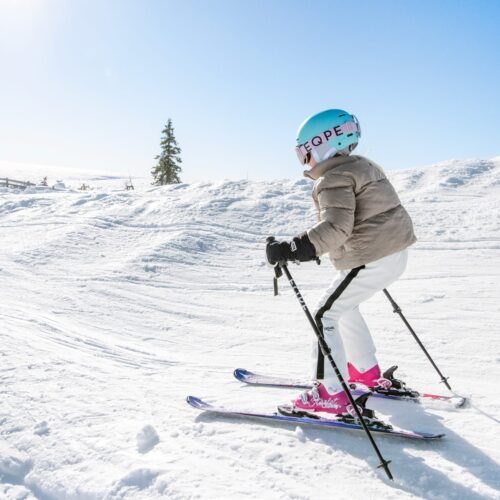 Barn åker skidor i solig backe med blå himmel och snölandskap i bakgrunden