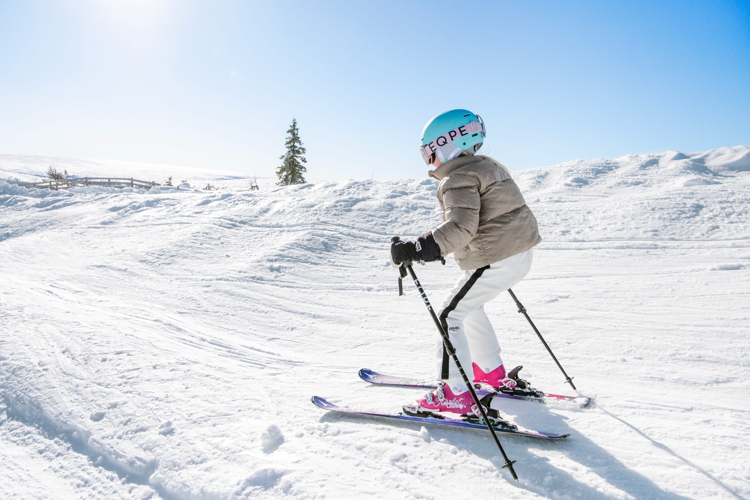 Børn på ski på en solrig skråning med blå himmel og snedækket landskab i baggrunden