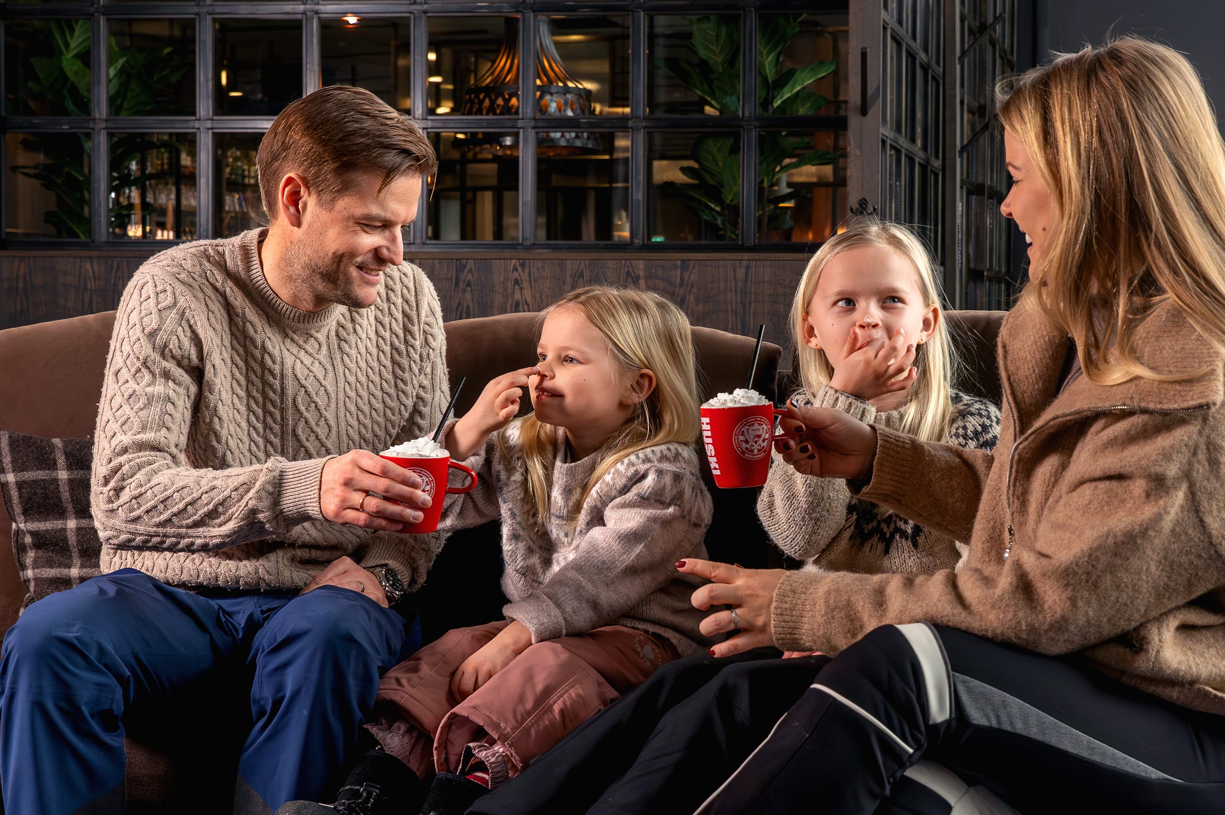 Fyra personer sitter i lounge och håller röda muggar med varm dryck och grädde.
