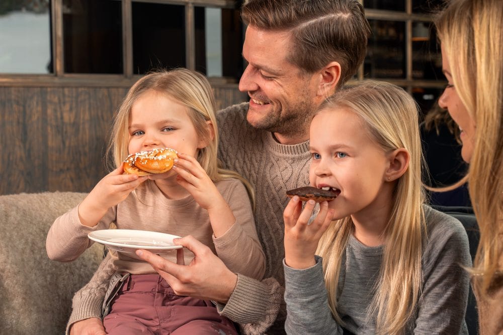 Två barn äter chokladbitar medan en vuxen håller tallrik i mysig miljö.
