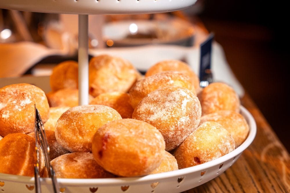 Närbild på fat med pudrade jordgubbsdonuts staplade på buffébord.
