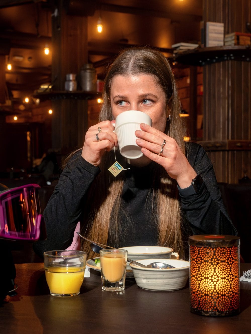 En person sidder ved et bord med te, juice, yoghurtskål og en tændt lanterne.