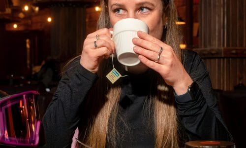 En person sidder ved et bord med te, juice, yoghurtskål og en tændt lanterne.