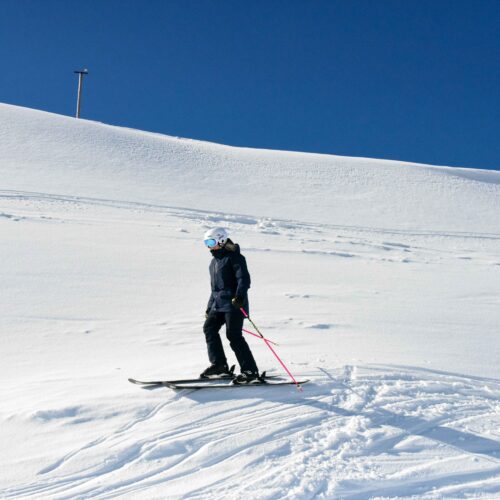 Skidåkare står på snötäckt fjällsluttning med blå himmel och spår i bakgrunden