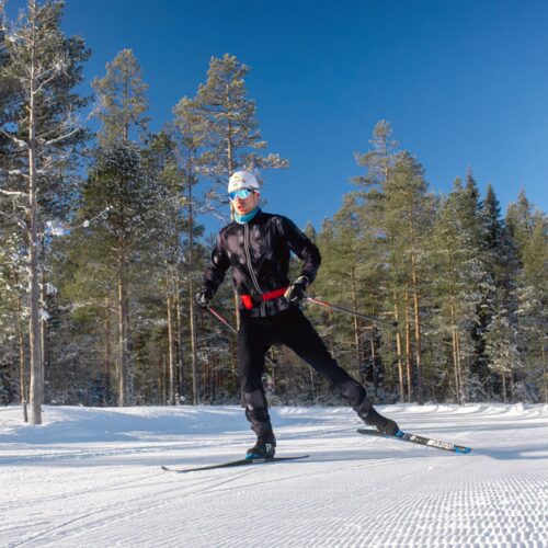Person åker skate-skidor på preparerat spår i soligt vinterlandskap med snötäckta träd