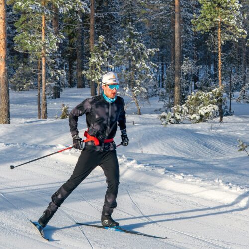En person står på skøjter på et præpareret spor i et solrigt vinterlandskab med snedækkede træer