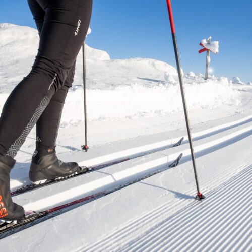 Person åker längdskidor på preparerat spår i soligt vinterlandskap med snö och blå himmel