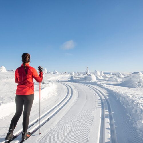 Person i röd jacka åker längdskidor på preparerat spår i snötäckt fjällandskap
