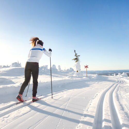 Person åker längdskidor på nypreparerade spår i öppet fjällandskap under klarblå himmel