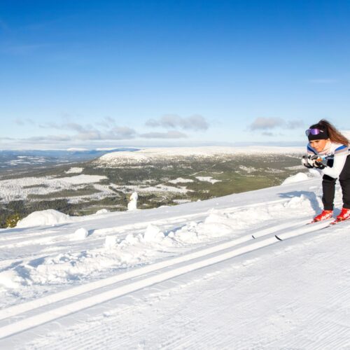 Person på langrendsski på nypræparerede spor i åbent bjerglandskab under klar blå himmel