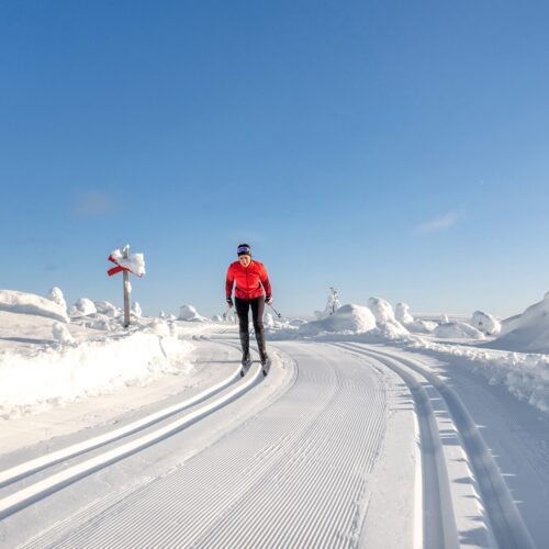 Person åker längdskidor på nypreparerade spår i öppet fjällandskap under klarblå himmel