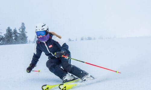 Skiers carving turns in open piste, white misty mountain environment, helmet, poles and yellow skis.