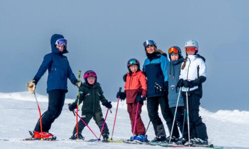 Family of six standing on ski slope with skis on.