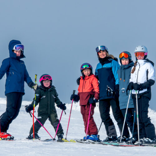 Familj bestående av sex personer står i skidbacke med skidor på.