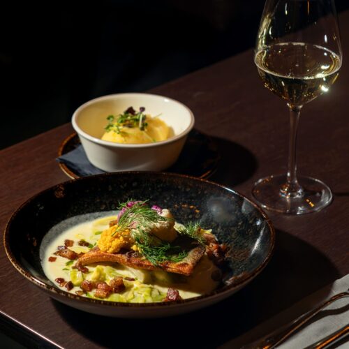 Fried fish fillet with dill, rum, creamy sauce and bacon bits in a black bowl.