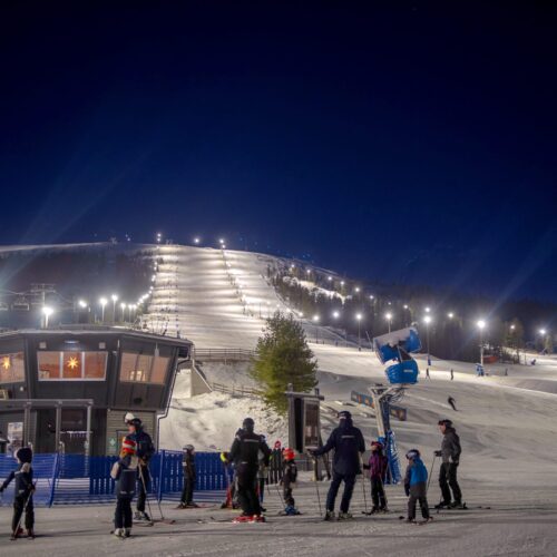 Oplyst skibakke til aftenskiløb med snekanoner og skiløbere ved foden