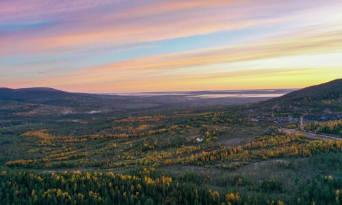 Höstlandskap med färgade träd och berg under mjuka pastellfärgade solnedgångsmoln