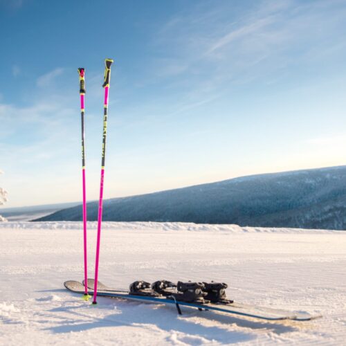 Två rosa skidstavar och skidor på snötäckt fjäll med blå himmel