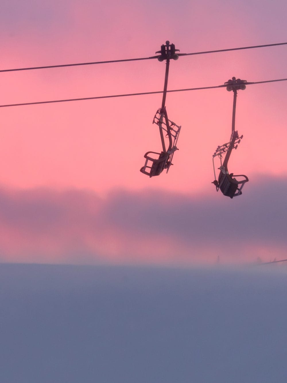 Två tomma stolliftar hänger mot rosa himmel vid solnedgång över snötäckt landskap