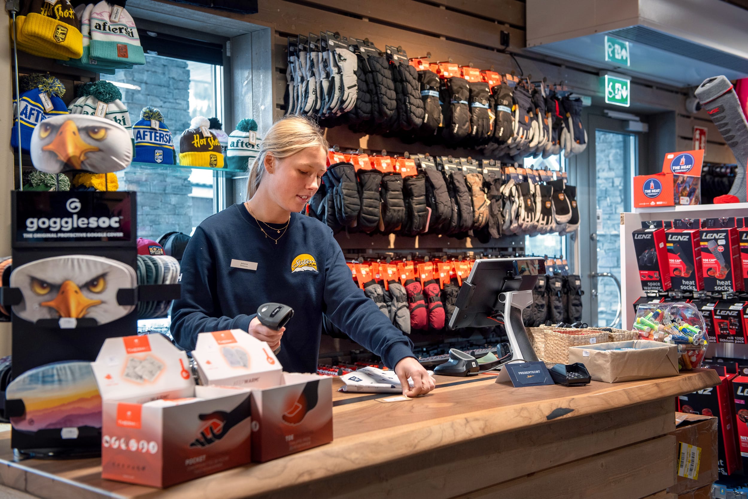 Kassadisk i skidshop med personal som skannar varor, vägg fylld med handskar och utrustning