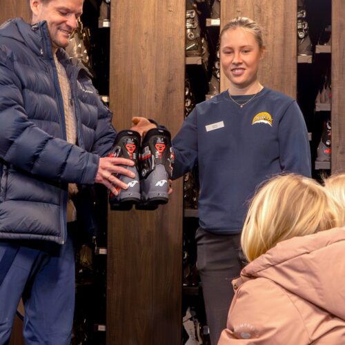 Personer i skiduthyrning håller i ett par pjäxor framför hyllor med skidutrustning