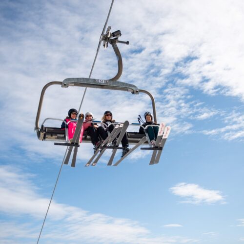 Four people sitting in ski lift against blue sky with light clouds