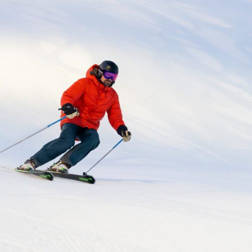 Person på slalomski i rød jakke på solrig, snedækket skibakke