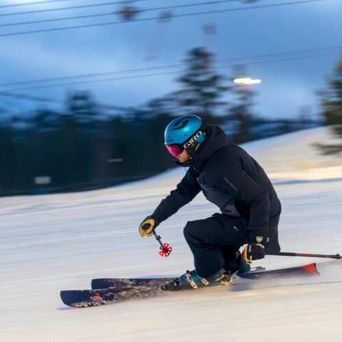 Skier in black gear and blue helmet turns fast on snow-covered slope