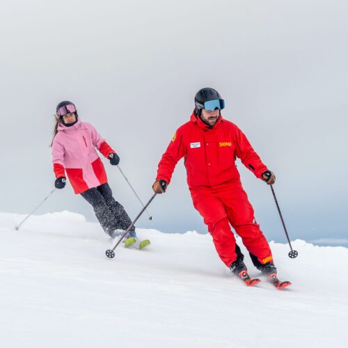 Skilærer i rødt udstyr underviser deltagere i lyserød jakke på snedækket skibakke