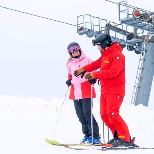 Skilærer i rødt udstyr underviser deltagere i lyserød jakke på snedækket skibakke