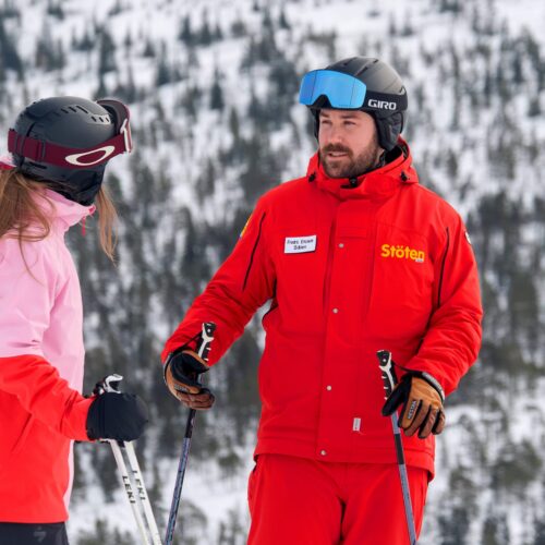 Skilærer i rødt udstyr underviser deltagere i lyserød jakke på snedækket skibakke