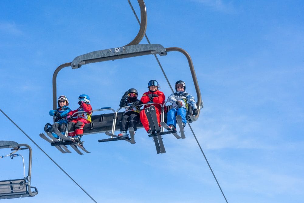 Five skiers sit in chairlift against clear blue sky at winter sports centre