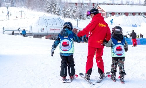 Instruktør hjælper to børn i skiskole ved liftområde i snedækket skisportssted