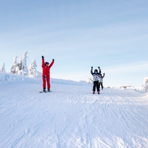 Ski school instructor and children skiing on sunny slope with snow covered trees around