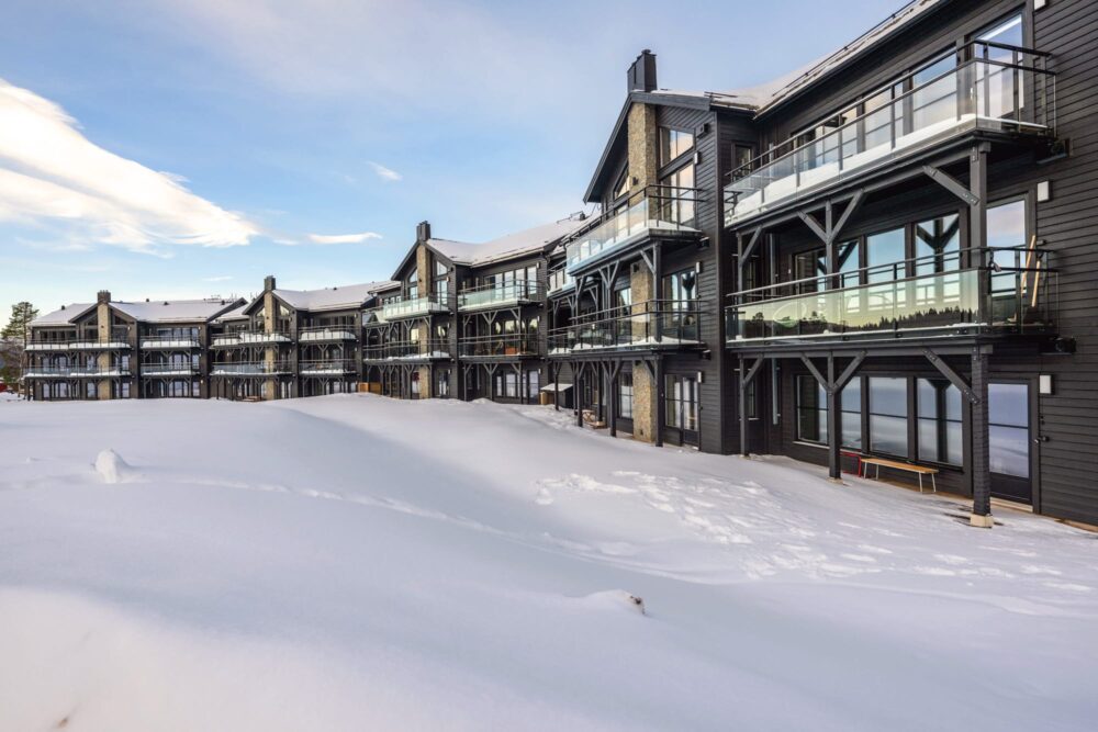 Modernt fjällhotell med svarta träfasader och stora glasbalkonger omgiven av djup snö.