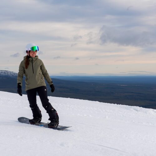 Snowboardere i grønne jakker kører på snedækket bjerg med skov og horisont i baggrunden