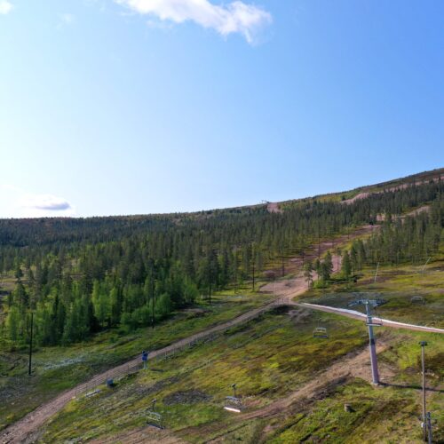 Green mountainside with chairlift poles and blue sky on a sunny summer day