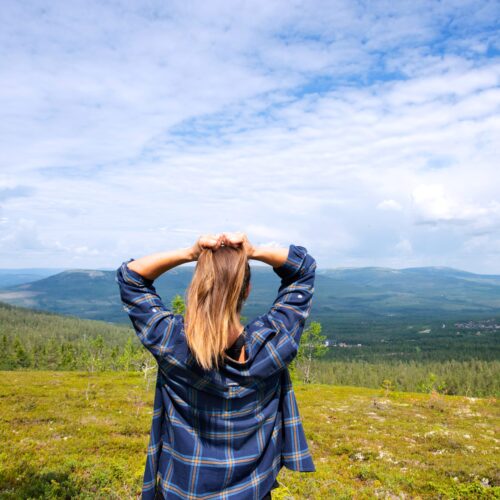 Person står på fjällhed med utsikt över gröna dalar och blå himmel med moln