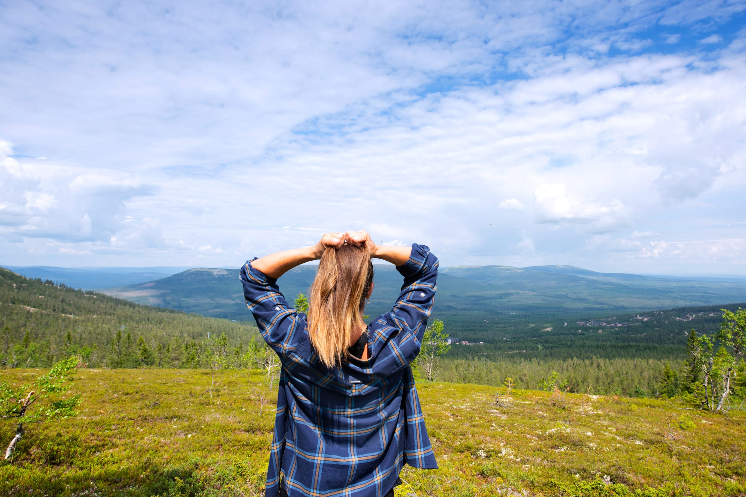 Person standing on mountain heath overlooking green valleys and blue sky with clouds
