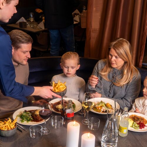 Tjenere sender skåle med chips til borde med varme retter, drikkevarer og stearinlys i en restaurant.