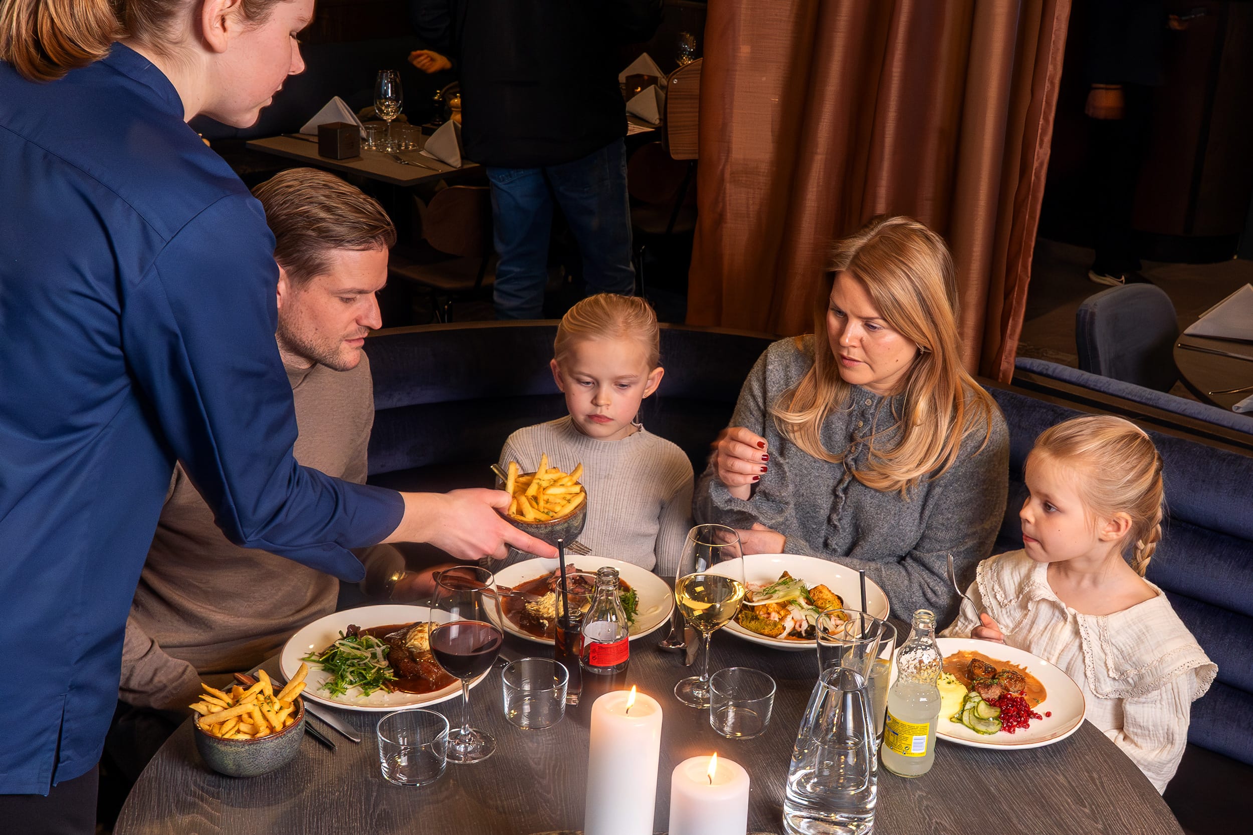 Tjenere sender skåle med chips til borde med varme retter, drikkevarer og stearinlys i en restaurant.